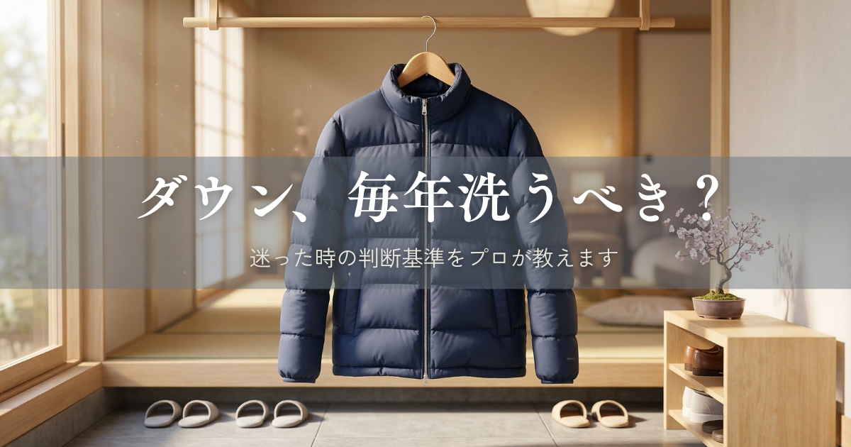 春の柔らかな日差しが差し込む清潔な玄関に、木製ハンガーで吊るされたネイビーのダウンジャケット。傍らには桜の花が生けられ、冬から春への衣替えをイメージした風景。