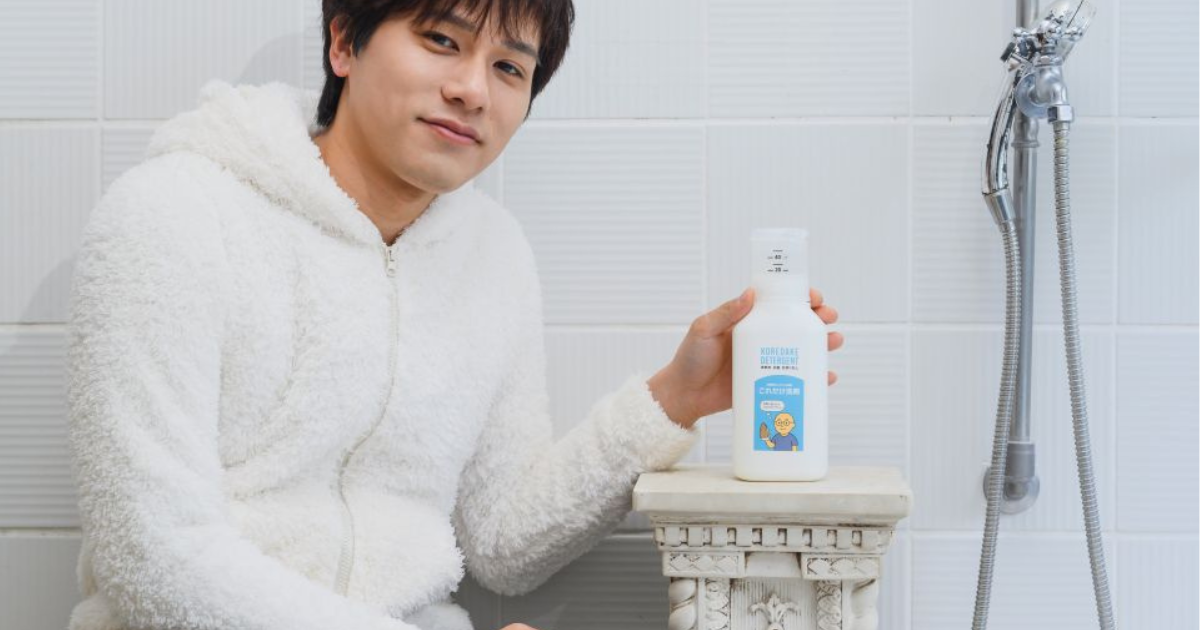 白いふわふわしたルームウェアを着た男性が、浴室のようなタイル背景で「これだけ洗剤」のボトルを手に持っている写真