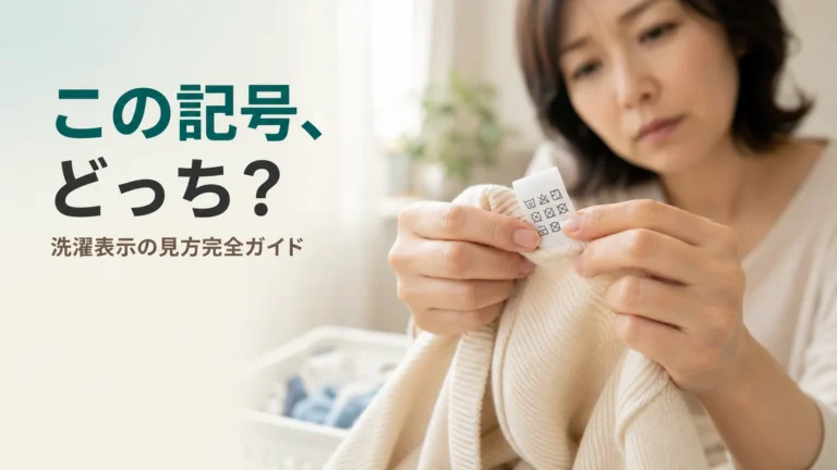 衣類の洗濯表示タグをつまんで、「この記号どっち?」と少し首をかしげながら見つめる女性の手元。家で洗えるか迷う、誰もが経験する日常の一場面を表現。北九州市小倉南区のファミリークリーニング(創業56年)が、新旧の洗濯マークの読み方をわかりやすく解説する記事のアイキャッチ。